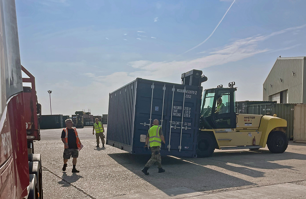 A yellow Hyster heavy forklift transports a blue shipping container at an outdoor logistics facility, while No. 4624 Movements Squadron workers supervise the operation.